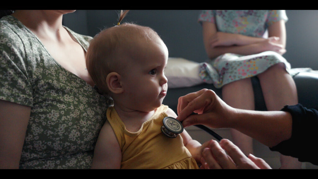 A toddler with a stethoscope pressed to their chest.