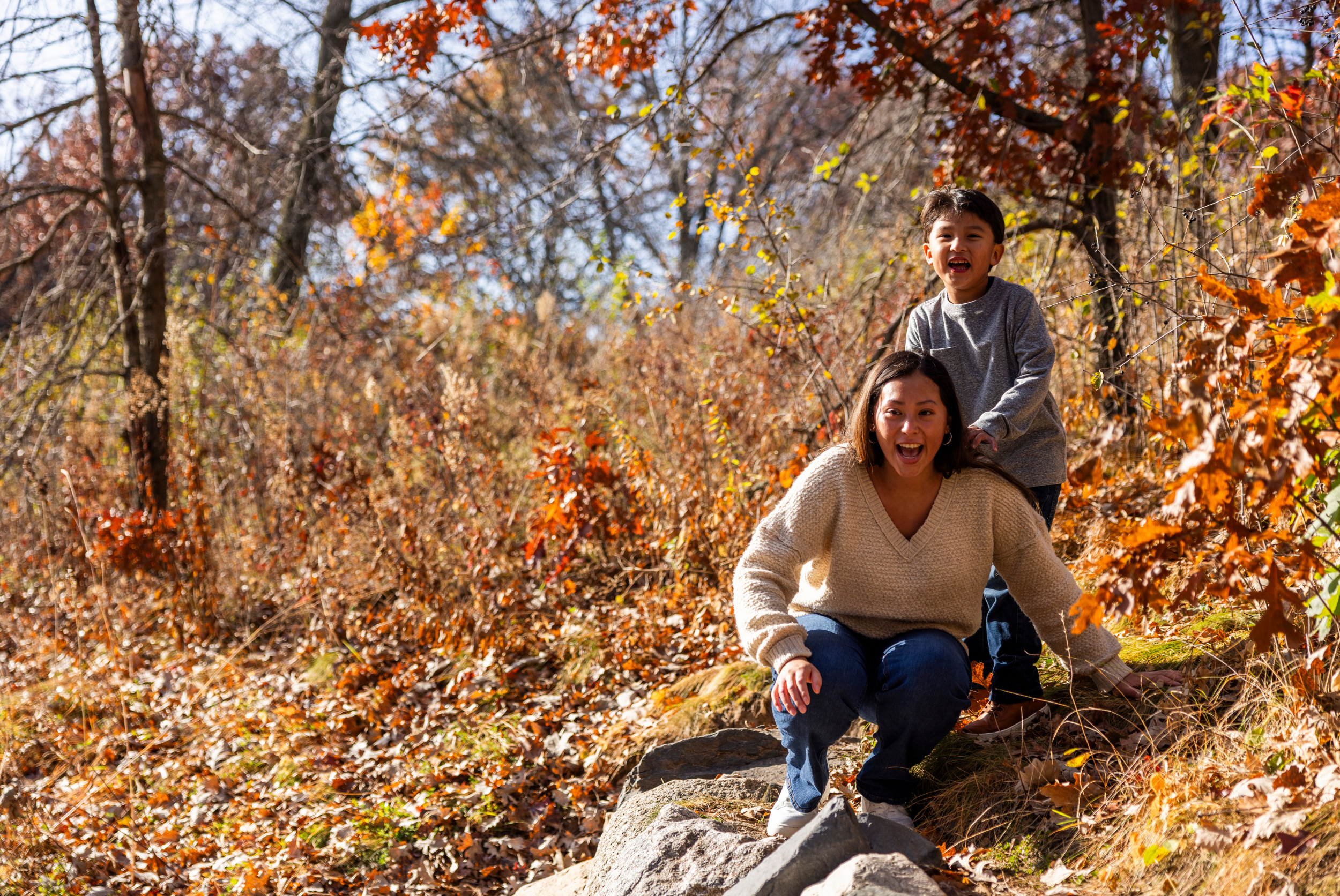 A woman and a child wearing sweaters, laughing outside in the fall.