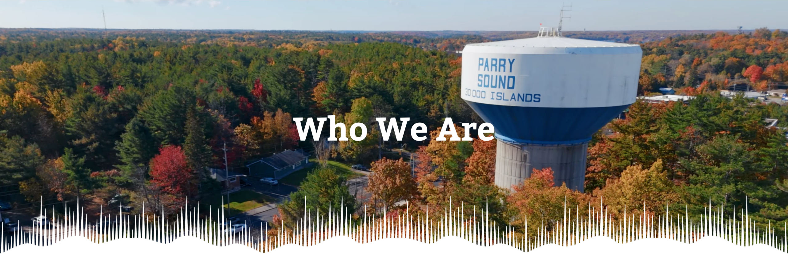 An aerial photograph of the Water Tower overlooking Bowes Street in Parry Sound. The tower is emblazoned with "Parry Sound, 30 000 Islands." The bottom of the picture is decorated with WPS OHT's Aurora motif.